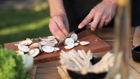 young man cutting mushrooms on wooden board in the garden close up