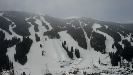 Aerial-Drone-Copper-Mountain-Colorado-Ikon-Epic-Pass-winter-spring-cloudy-snowy-early-morning-first-light-gray-bird-half-pipe-chairlift-ski-runs-center-village-cinematic-slowly-backwards-down-motion