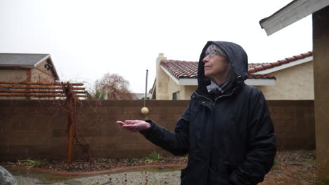 A-middle-aged-woman-in-a-winter-storm-wearing-a-rain-coat-and-feeling-the-snow-and-raindrops-with-her-hand-in-slow-motion