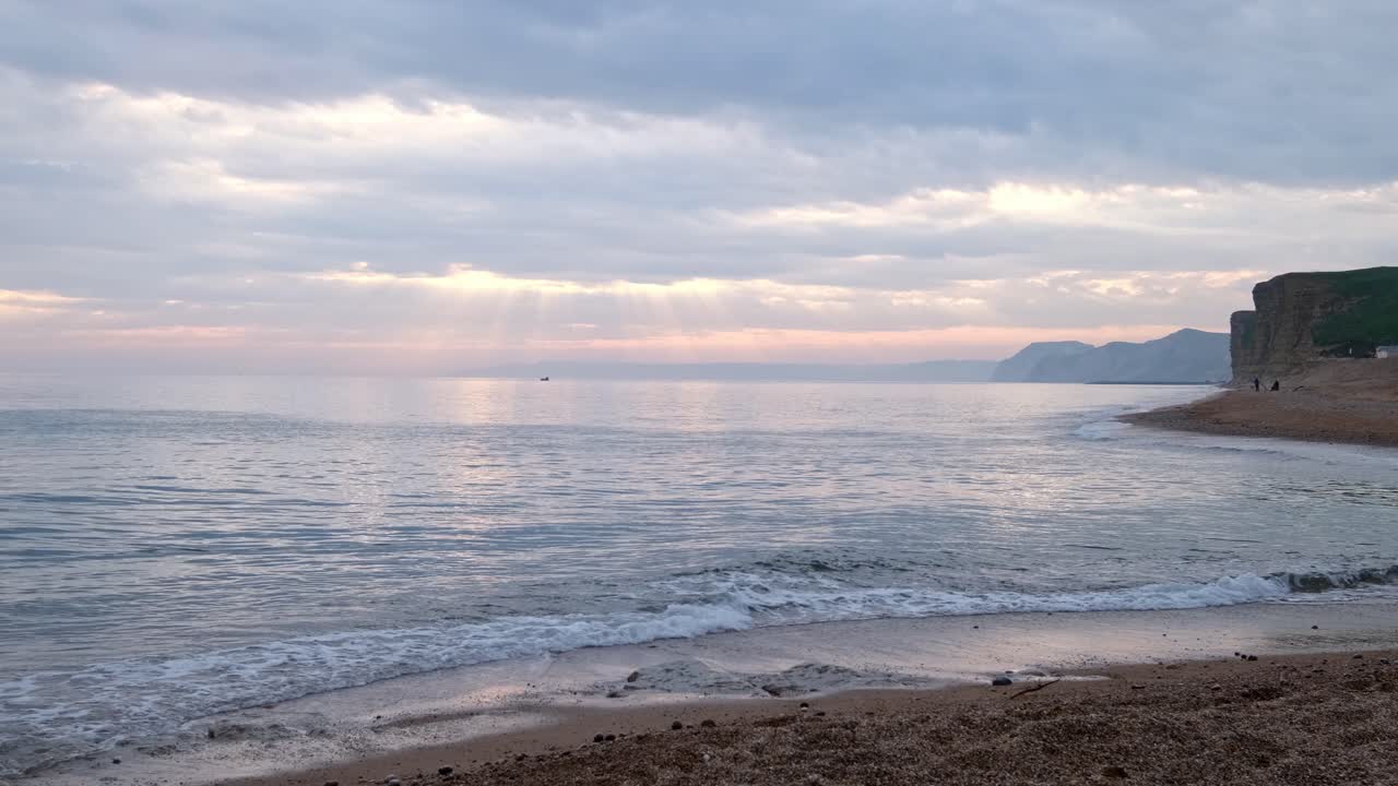 Jurassic Coast beach scene captures waves in slow motion just after sunset. Dorset. Blue sea with various cliffs along the shoreline.