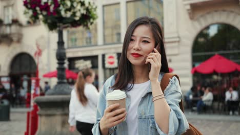 Beautiful-Young-Woman-Talking-Joyfully-On-The-Mobile-Phone-And-Drinking-Coffee-To-Go-While-Walking-City-Center