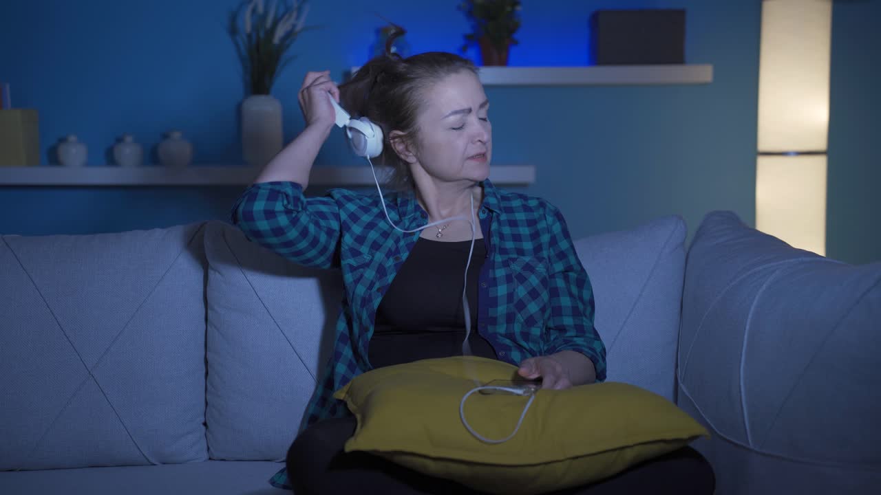 슬프고 불행한 여자가 밤에 집에서 음악을 듣고 있습니다.