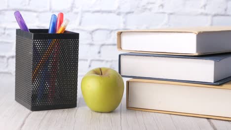 books, pens, and an apple on a desk