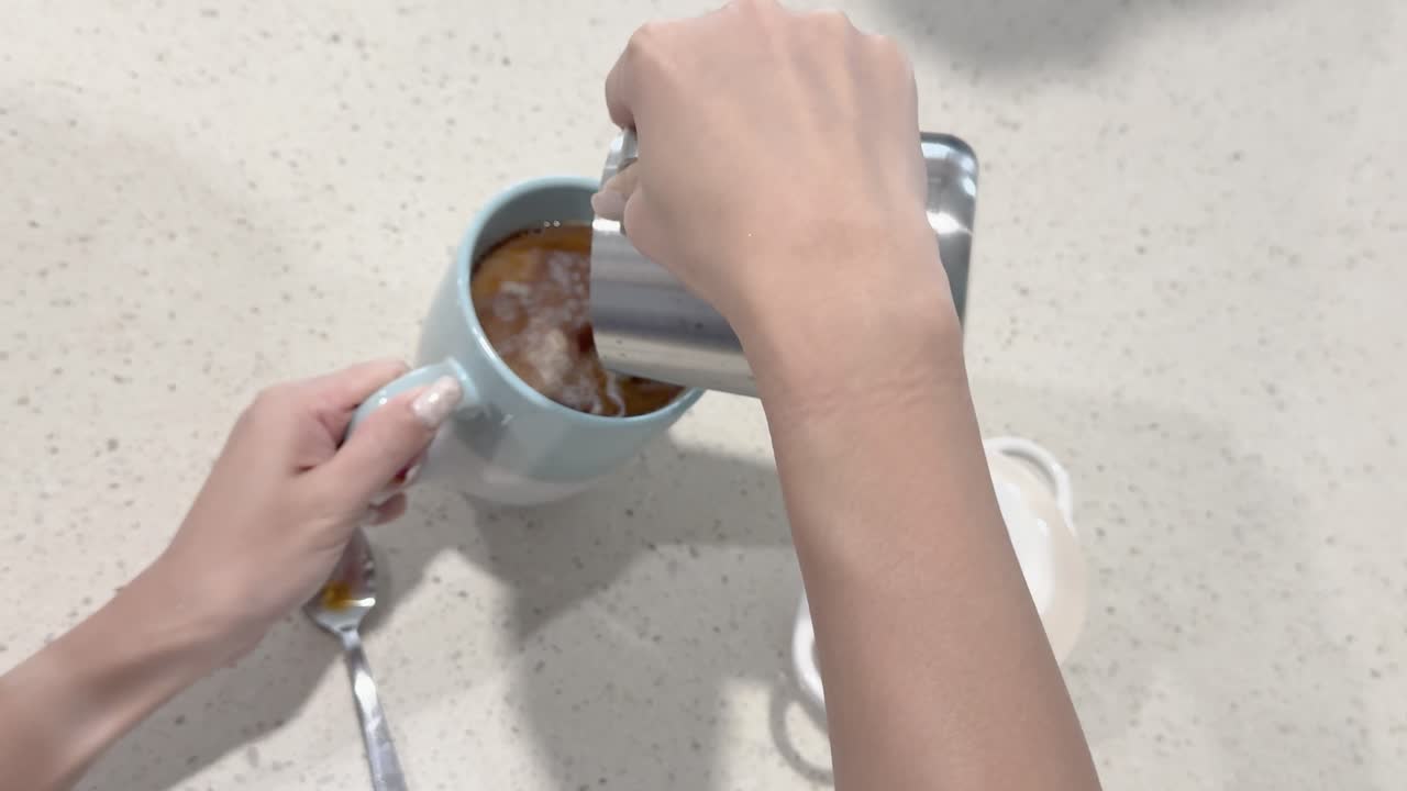 A person pours milk into a coffee cup on a countertop, creating a swirling effect