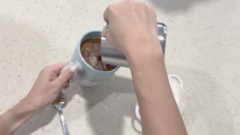 a person pours milk into a coffee cup on a countertop, creating a swirling effect