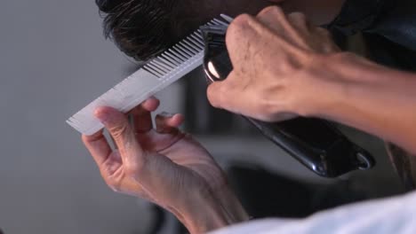 white comb and battery powered hair clipper used to trim and level edges of black hair on rear right of head, filmed in closeup shot in vertical handheld slow motion style