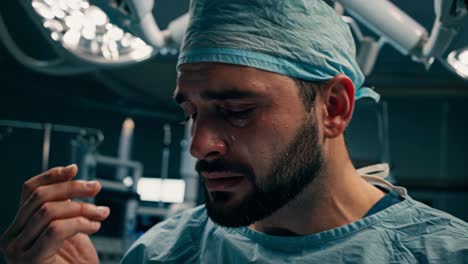 a distressed surgeon stands in an operating room, visibly affected by the intensity of the situation. wearing surgical scrubs and a cap, he wipes his face while tears well in his eyes. the sterile environment of the hospital is filled with medical equipment and bright overhead lights. the emotional