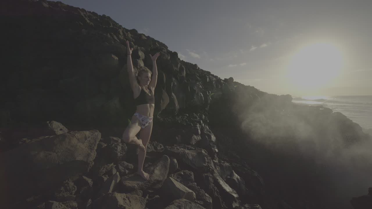 Woman practicing yoga on a rocky cliff overlooking the ocean