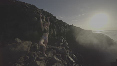 woman practicing yoga on a rocky cliff overlooking the ocean