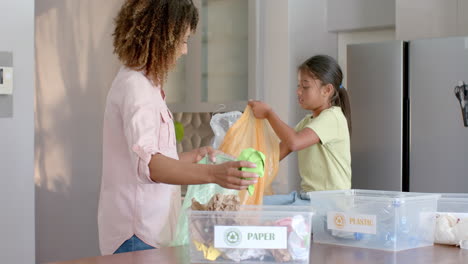 happy biracial mother and daughter sorting rubbish for recycling in kitchen, slow motion