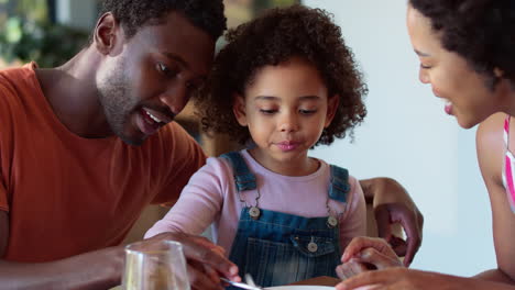 Family-Shot-With-Parents-And-Daughter-At-Home-Having-Breakfast-Spreading-Jam-On-Bread-At-Table