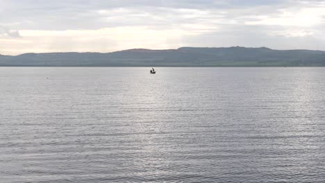 a small fishing canoe out in the distance on lake victoria in the early morning