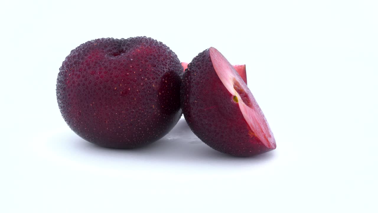 uno entero, un medio cortado y una pequeña parte de ciruelas púrpuras con gotas de agua. carne roja en el interior. girando en la mesa giratoria. aislado en el fondo blanco. primer plano. macro.
