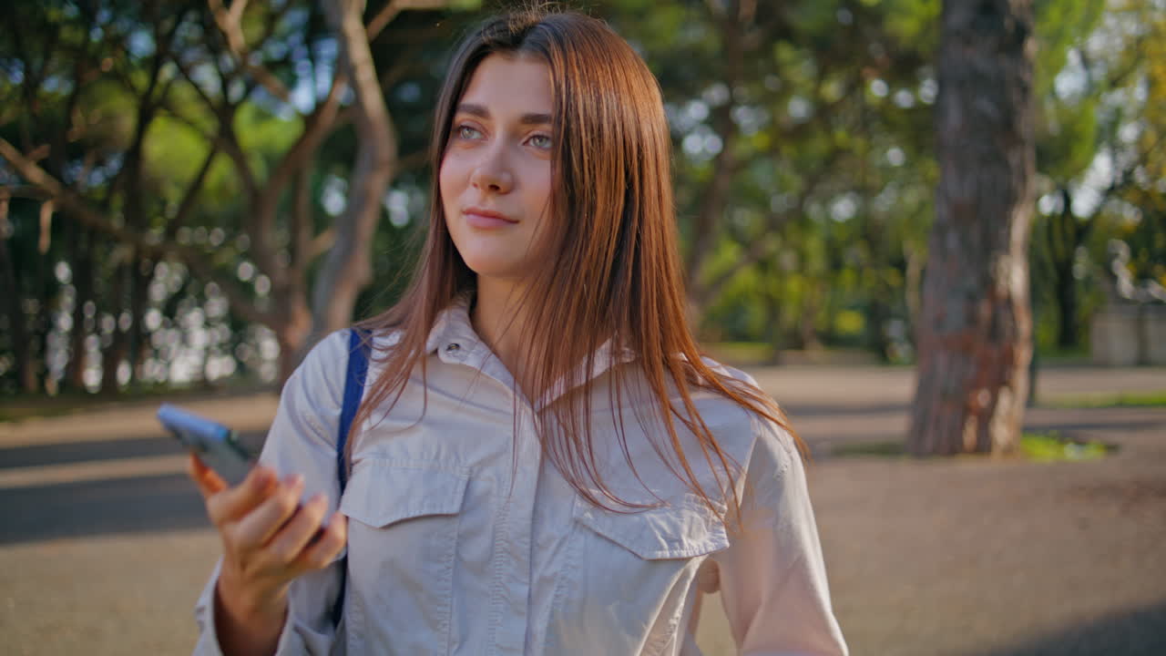 Estudiante sonriente conversando por celular de pie en un hermoso parque verde. Mujer sonriente.
