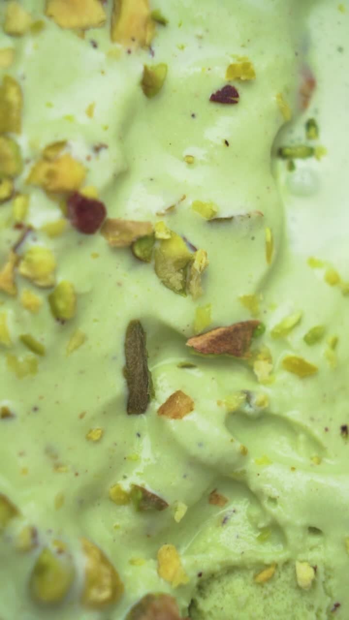 A vertical close-up showcasing gourmet pistachio ice cream with a topping of raw green nuts, emphasizing freshness and indulgence