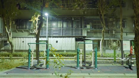 Push-in-past-foreground-tree-towards-exercise-park-in-taipei-outside-apartment-building-at-night