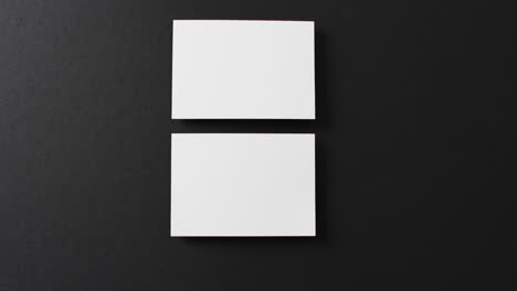 Overhead-view-of-two-white-business-cards-arranged-on-black-background,-copy-space,-slow-motion