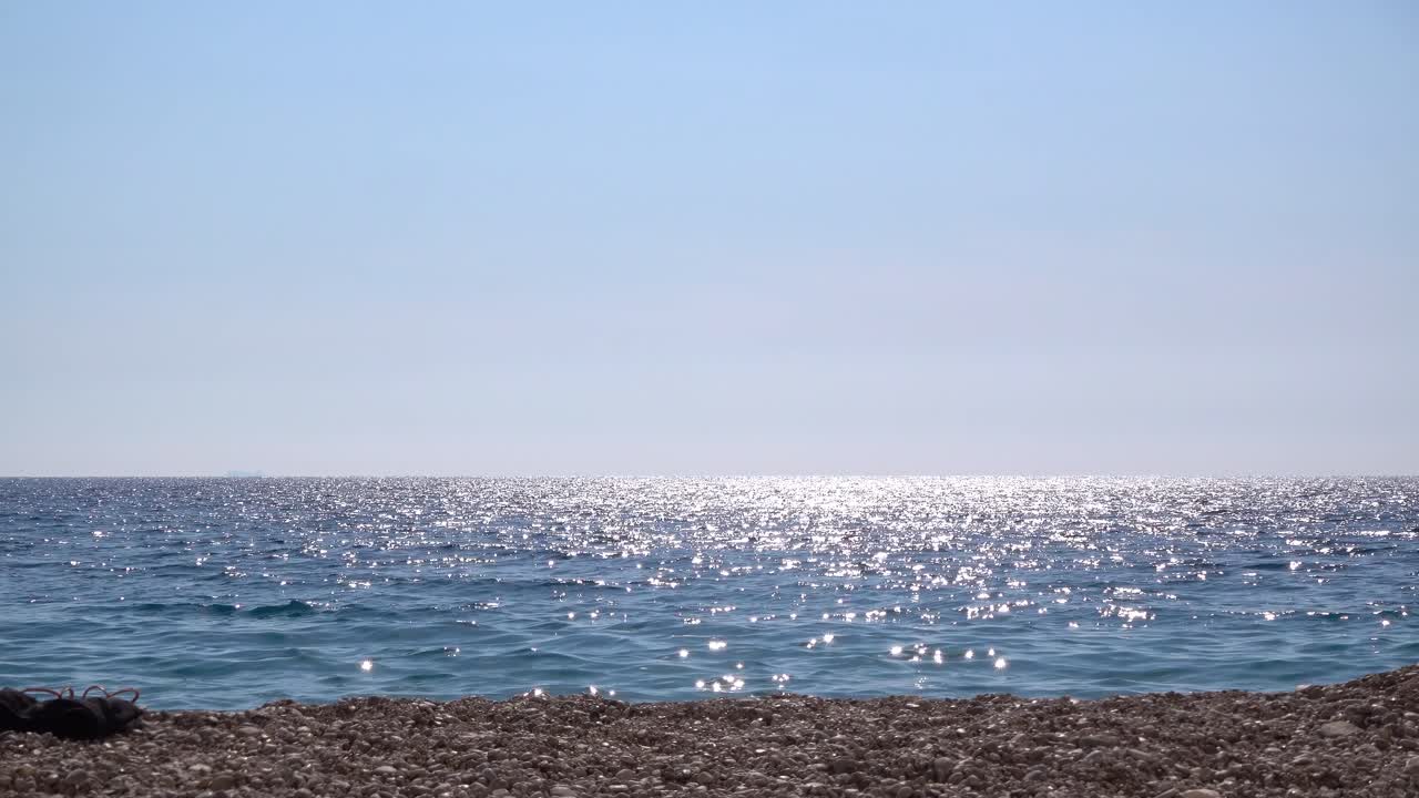 수평선 위로 반짝이는 태양이 있는 바위 해변과 바다의 낮은 각도