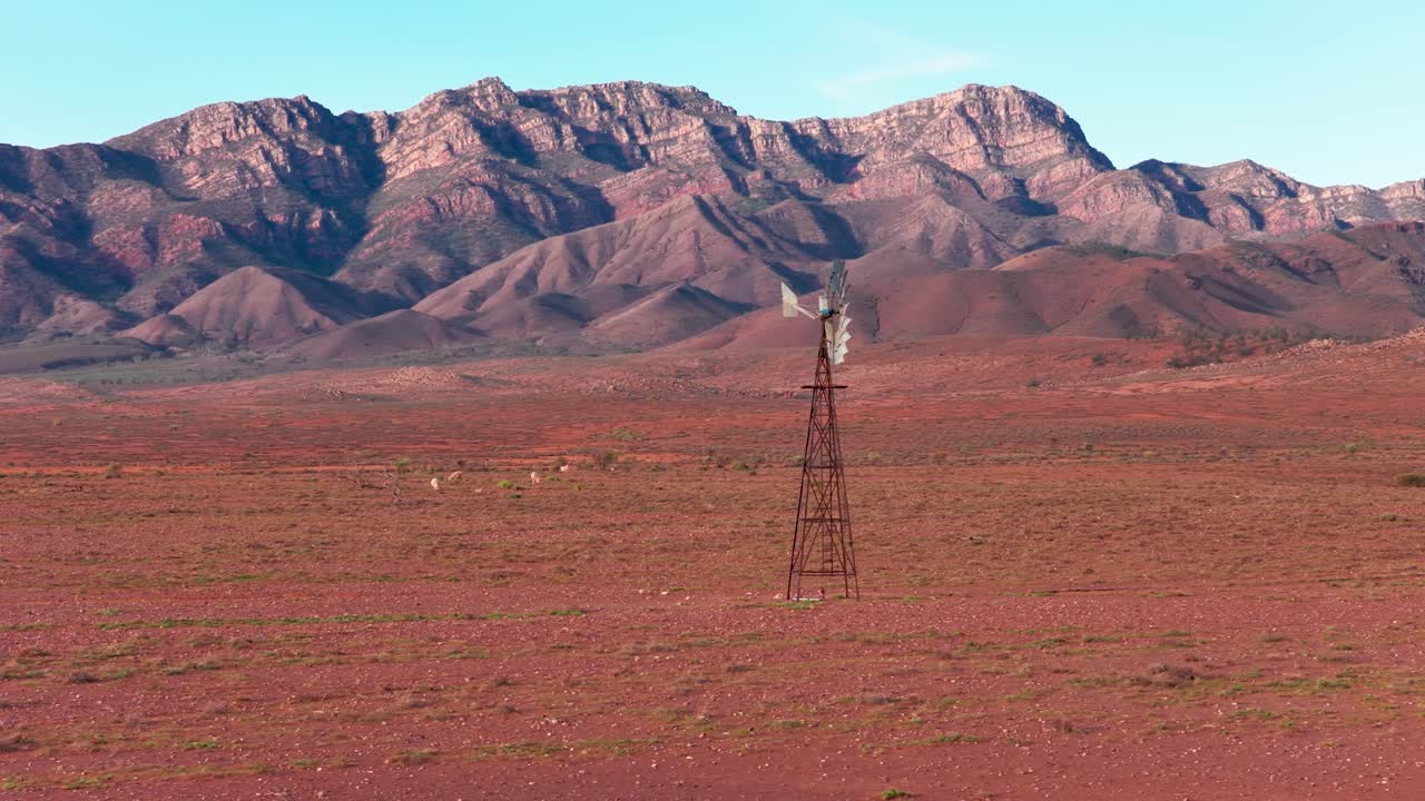 Drone telephoto shot with enlarged Flinders Ranges mountains behind isolated windmill, South Australia