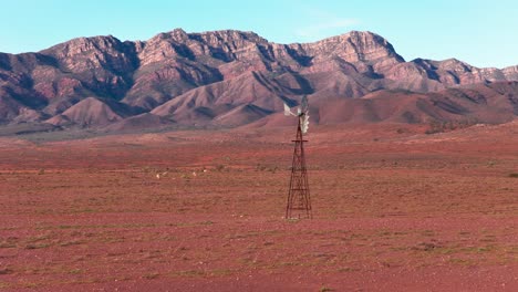drone telephoto shot with enlarged flinders ranges mountains behind isolated windmill, south australia