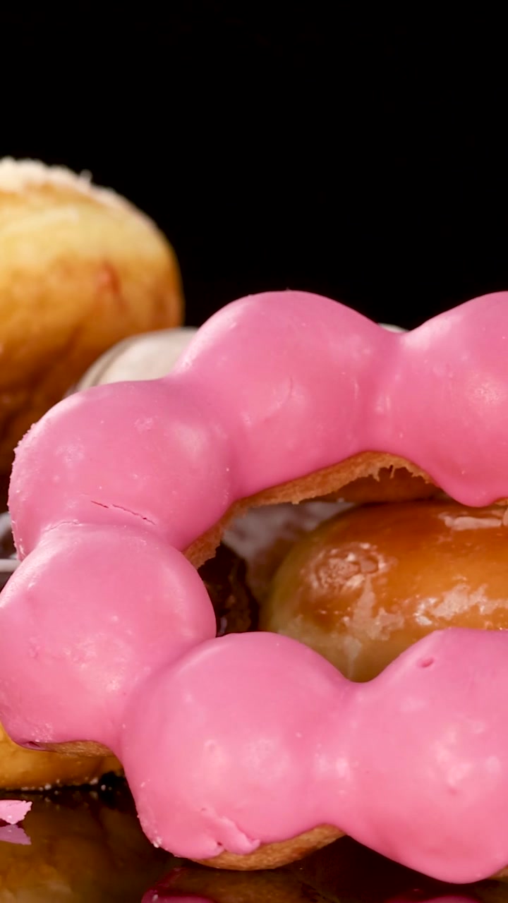Una vibrante selección de donas glaseadas y cubiertas gira lentamente sobre una superficie oscura reflectante.
