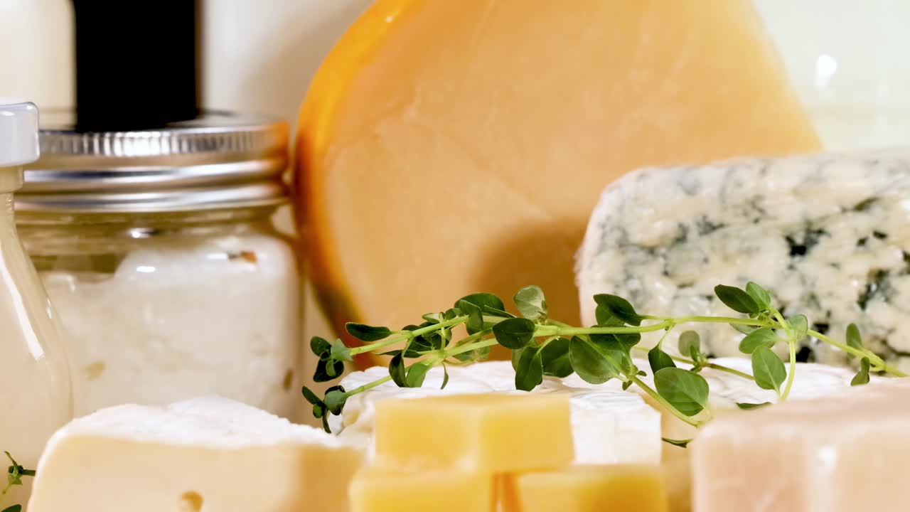 Close-up of various cheeses and jars with herbs on a black background.