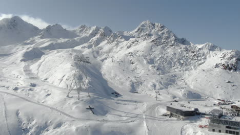 Christian-cross-on-the-side-of-the-hill-aerial-panoramic-shot-of-snowy-mountains-in-ski-resort-lighting-by-sun---Kauntertal,-Austria