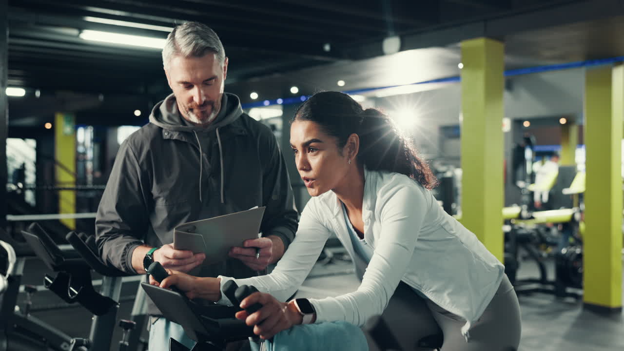 A woman works out on a stationary bike with her trainer present