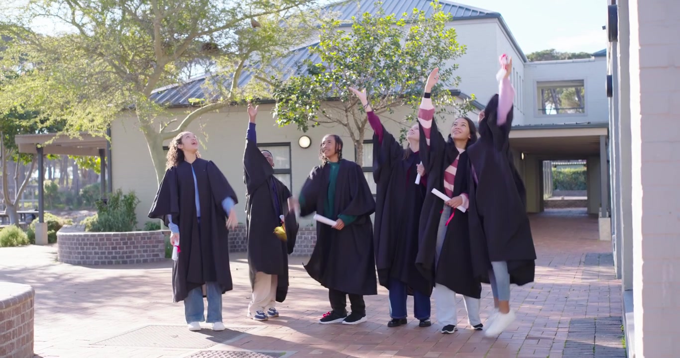 Diversi laureati in toga entrano da destra, radunandosi nel cortile, mostrando i diplomi, lanciando i cappelli e festeggiando.
