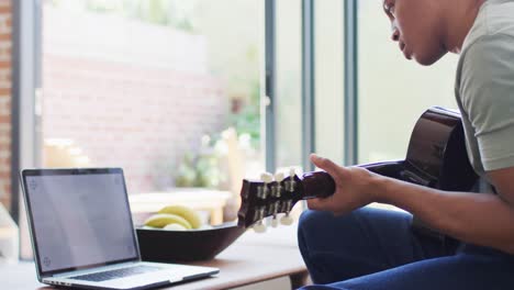 african american man plays guitar and singing, using laptop at home