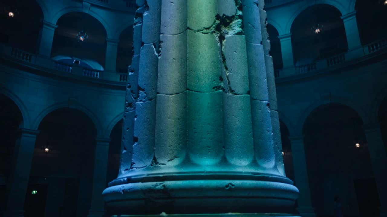 Panning camera revealing large weathered column in rotunda, highlighting cracks and teal light