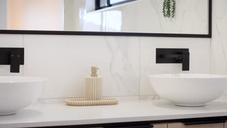 panorámica de primer plano a través de modernos doble vanidad redondeados cuencos de mármol y verde beige textura jabón dispensar plato, piezas de acento negro