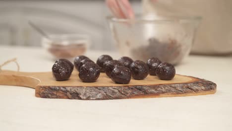 bottom top shot of homemade round chocolate sweets on the wooden cooking board in the foreground. woman's hand putting a candy onto the board. close-up demonstration video