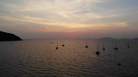 Flight-over-the-ocean-and-boat-with-sunset-and-mountains-in-the-background