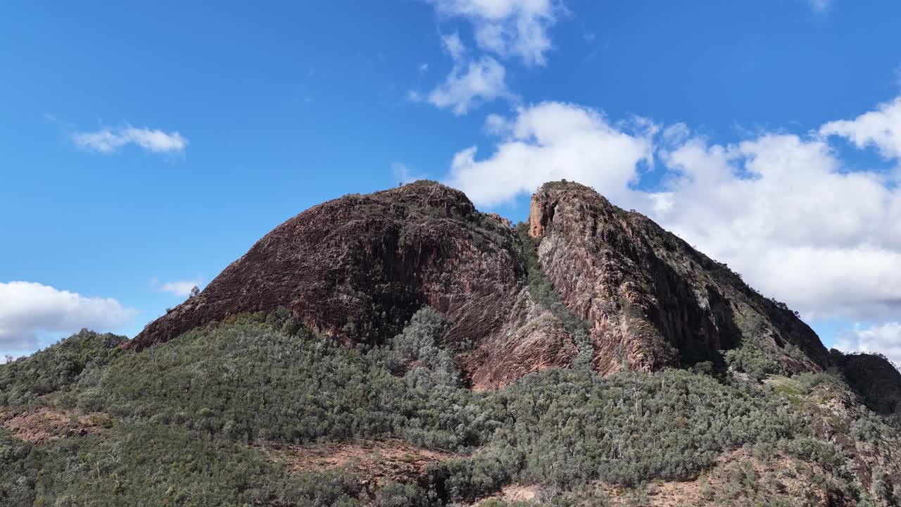 A slow daylight pan reveals Split Rock’s rugged peak and forested slopes under a bright blue sky in Warrumbungle National Park, Australia
