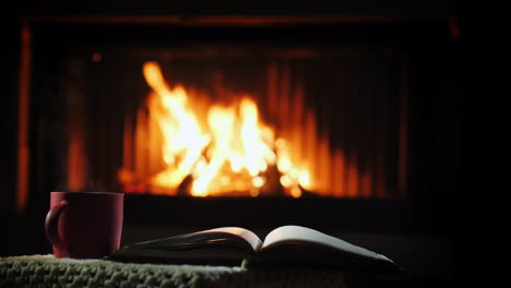 a book and a cup of hot haunted on a table near the fireplace winter leisure concept