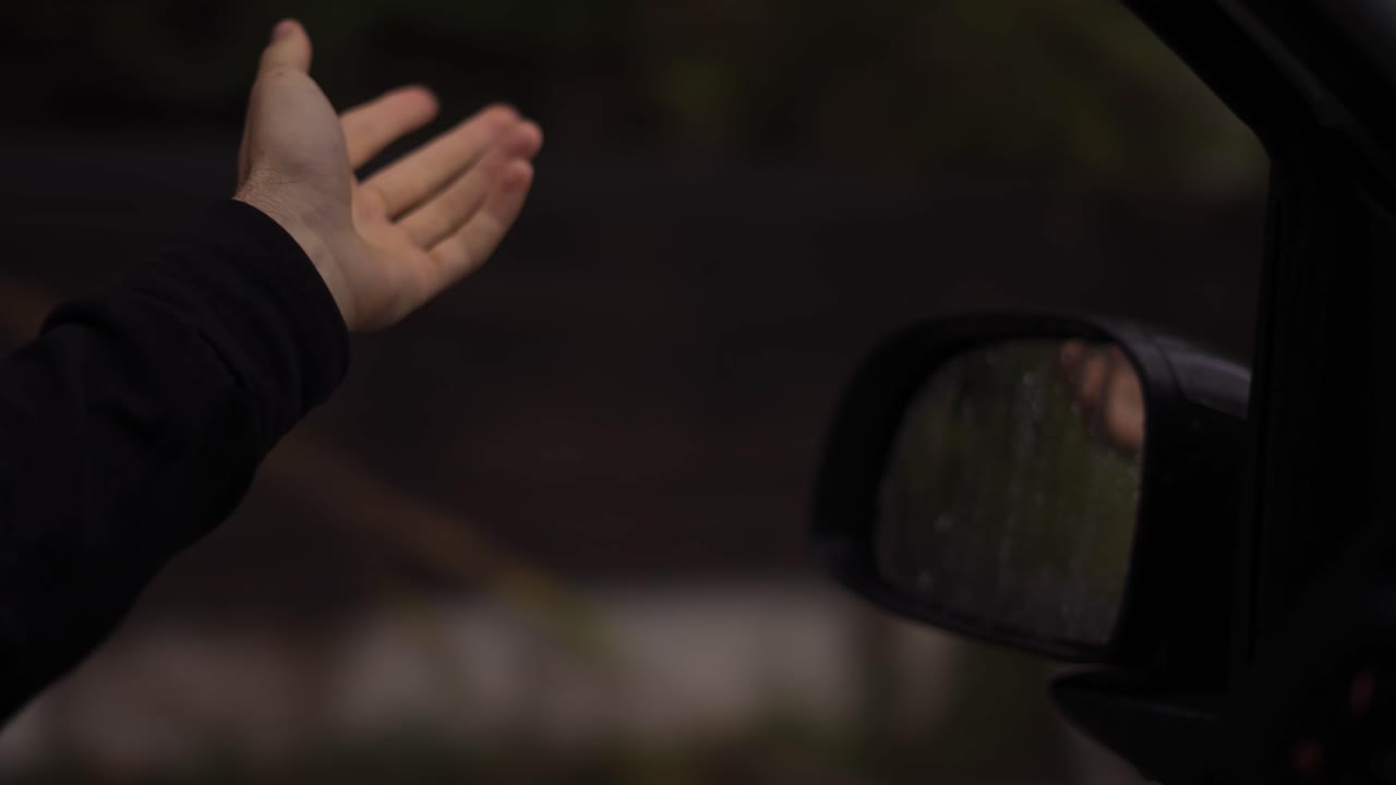 A man's hand is catching the rain out while driving a car on a rainy day, slow motion