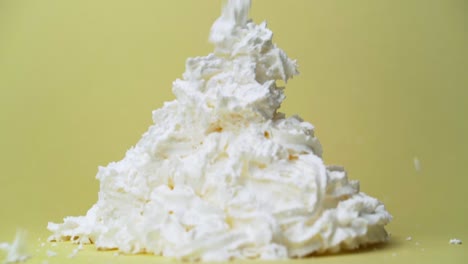 whipped cream can spraying into large pile panning down follow slow motion with yellow studio backdrop