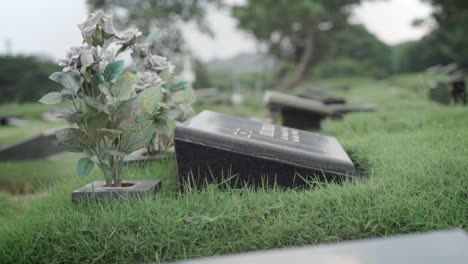 Black-granite-memorial-plaque-at-cemetery-and-vase-with-artificial-flowers,-close-up