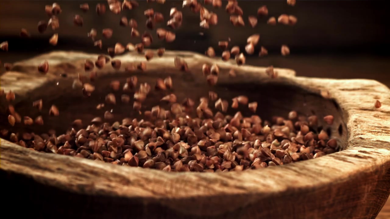 Grani di grano saraceno che cadono in una ciotola di legno rustica.
