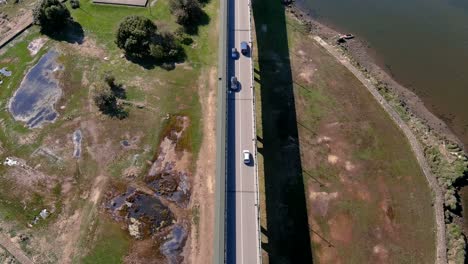 Cars-driving-over-the-bridge-over-the-Ulla-River-with-Viking-and-industrial-boats,-the-ruins-of-the-castle-towers,-sunny-afternoon,-rolling-drone-shot-down-zenithal