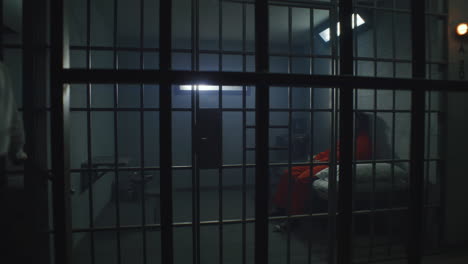 prison officer with police baton watches criminals in prison cells