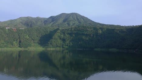 Drones-Vuelan-Sobre-La-Superficie-Del-Agua-Del-Lago-Con-Colinas-Y-Montañas-Al-Fondo