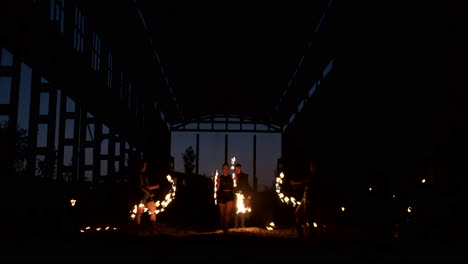 A-group-of-people-with-fire-and-torches-dancing-at-sunset-in-the-hangar-in-slow-motion.-Fire-show.