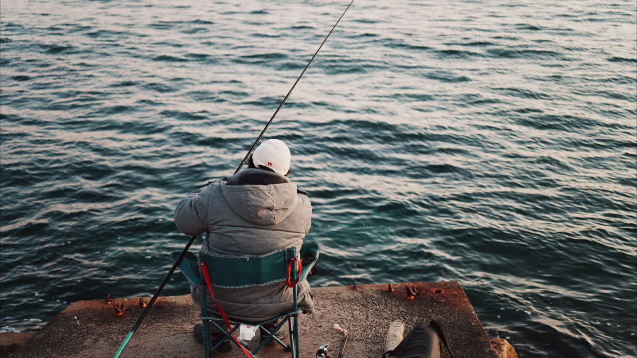 Man in winter clothes on a chair fishing in the sea in the south of France
