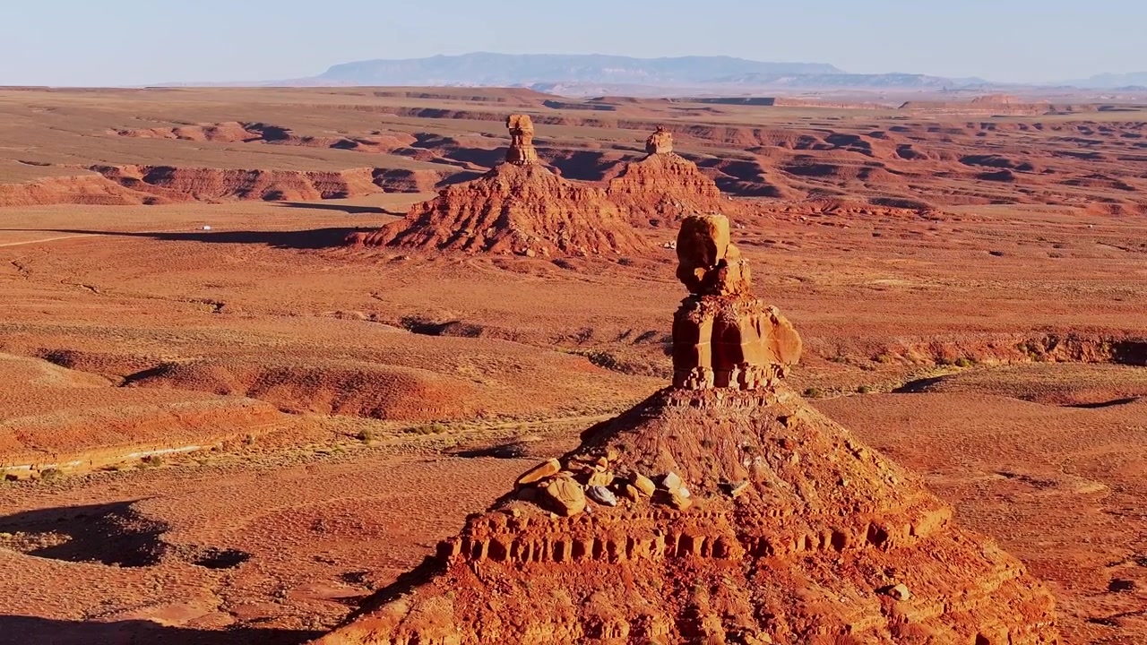 Drone pulls back past a close sandstone formation at Valley of the Gods, Utah, revealing Rooster Butte and the vast red desert stretching to distant mountains