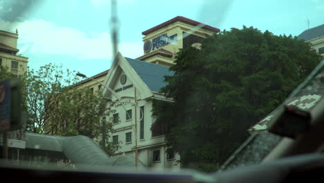 Edificio-Del-Hospital-Pusrawi-Revelado-Como-Se-Ve-Desde-El-Interior-Del-Espejo-Del-Coche-Del-Conductor,-Lluvioso-Afuera,-Gotas-De-Lluvia-En-La-Ventana-Exterior-Del-Coche