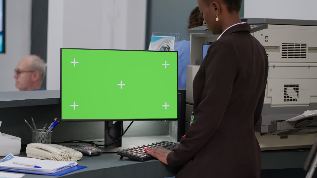 Businesswoman working at reception desk with green screen computer