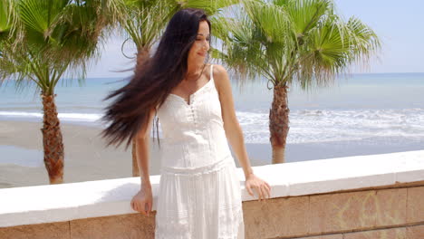 woman in white dress leaning against beach wall