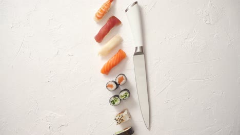 Various-sushi-rolls-with-Japanese-knife-on-white-stone-slate-background